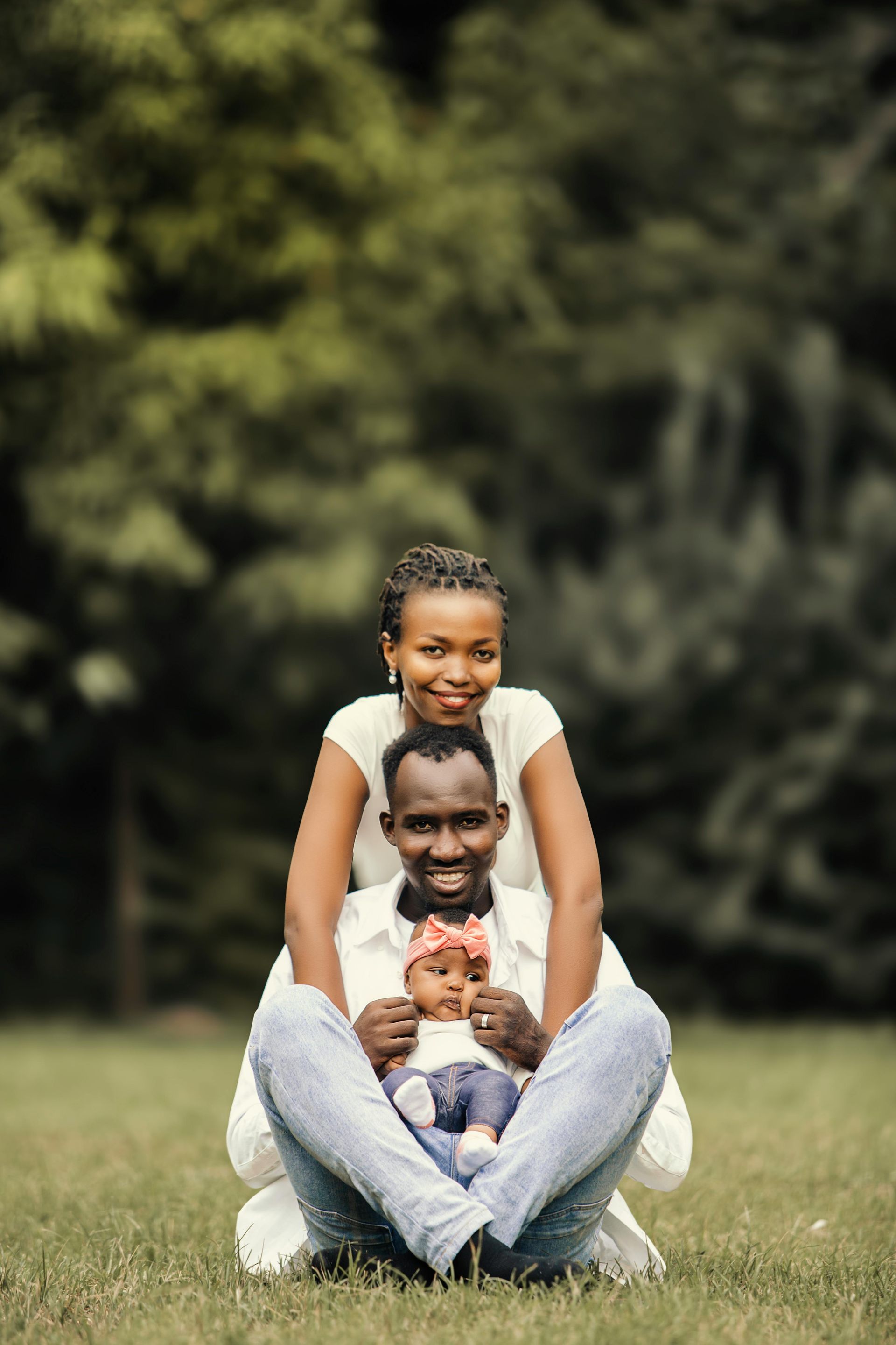 A man and woman are sitting on the grass with a baby.