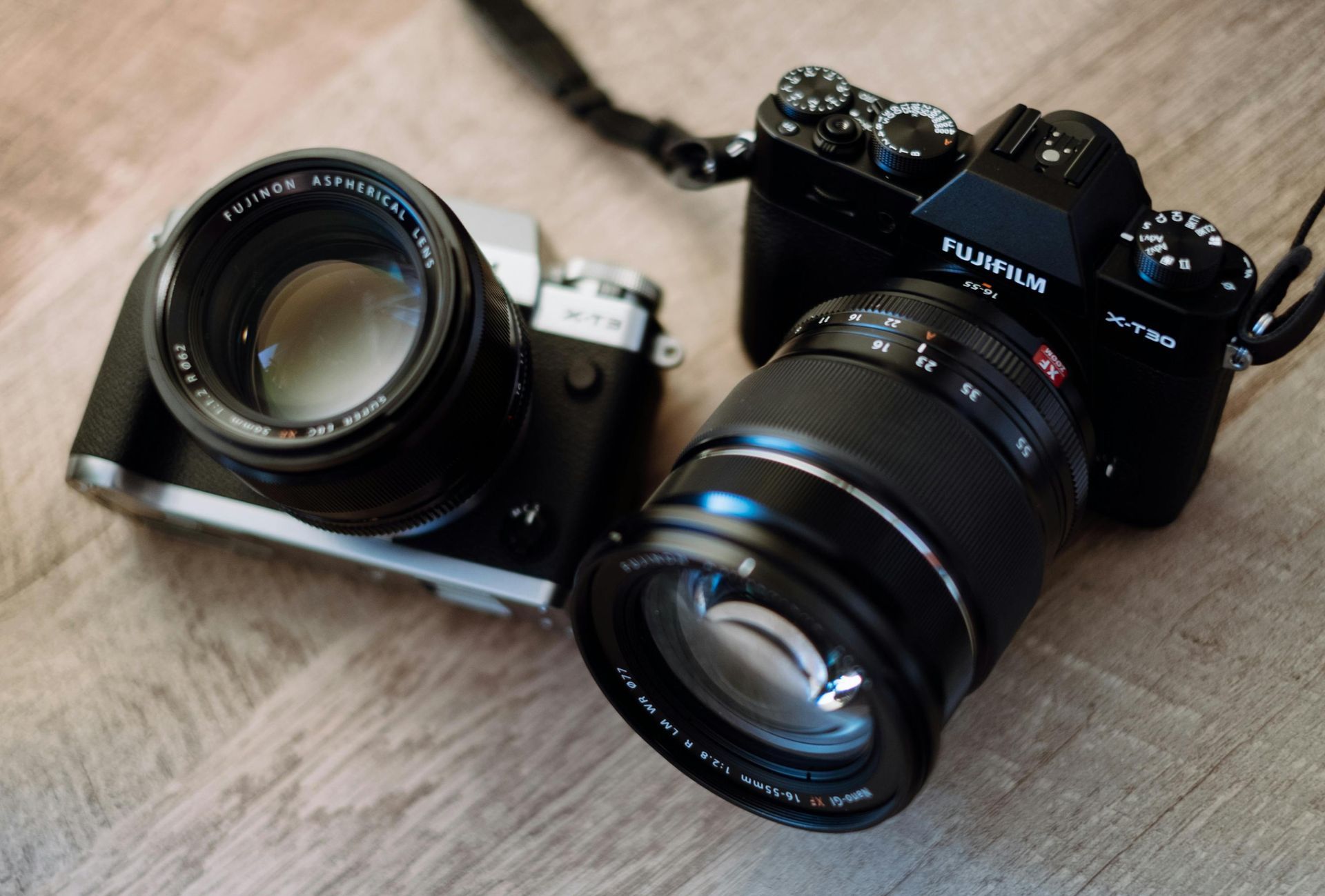 Two black cameras with lenses on a wooden surface.