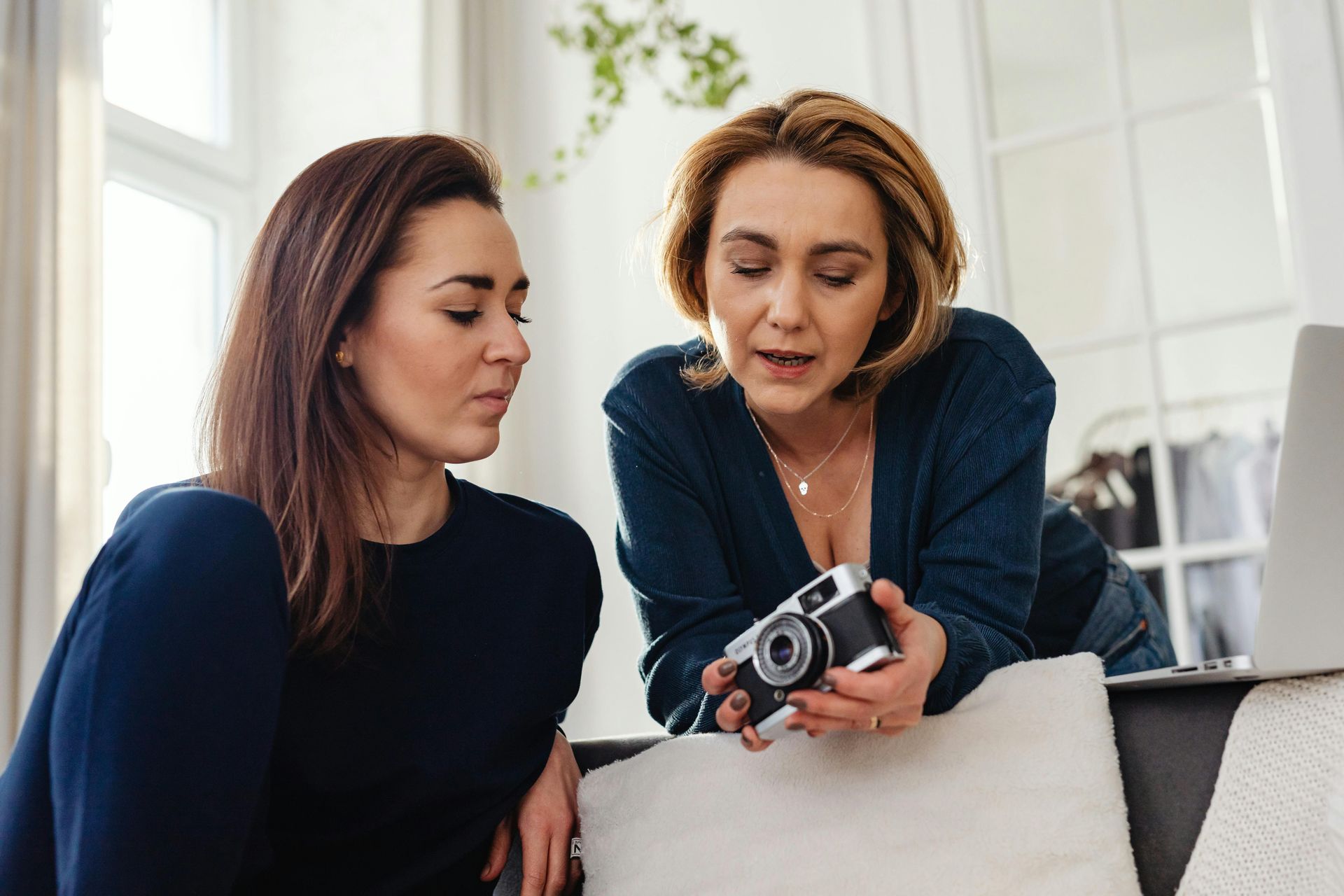 Two women examining a vintage camera indoors. One points, while the other observes with focused expression.