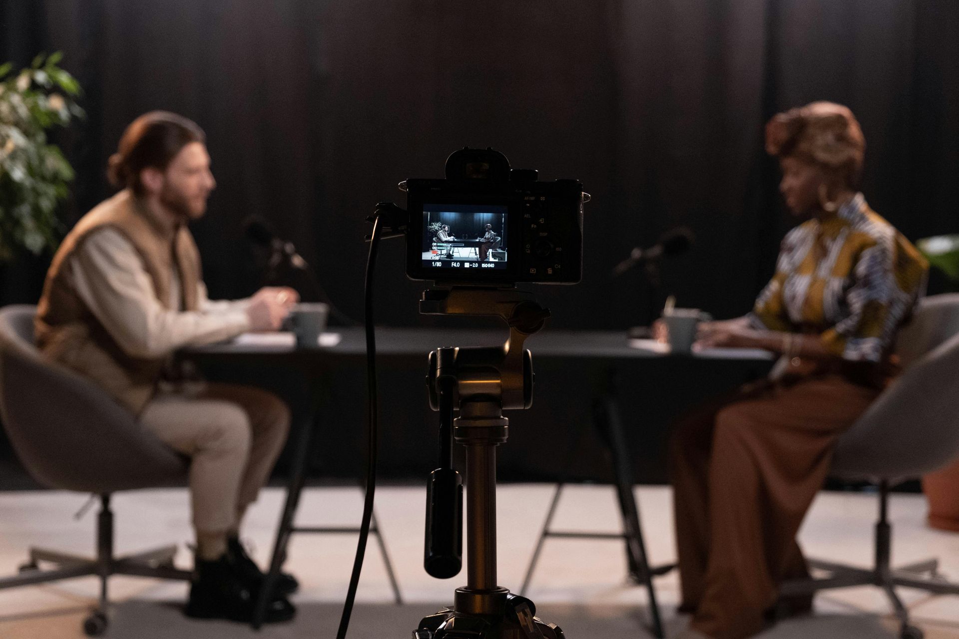 Camera recording two people at a table; man and woman in a studio setting.
