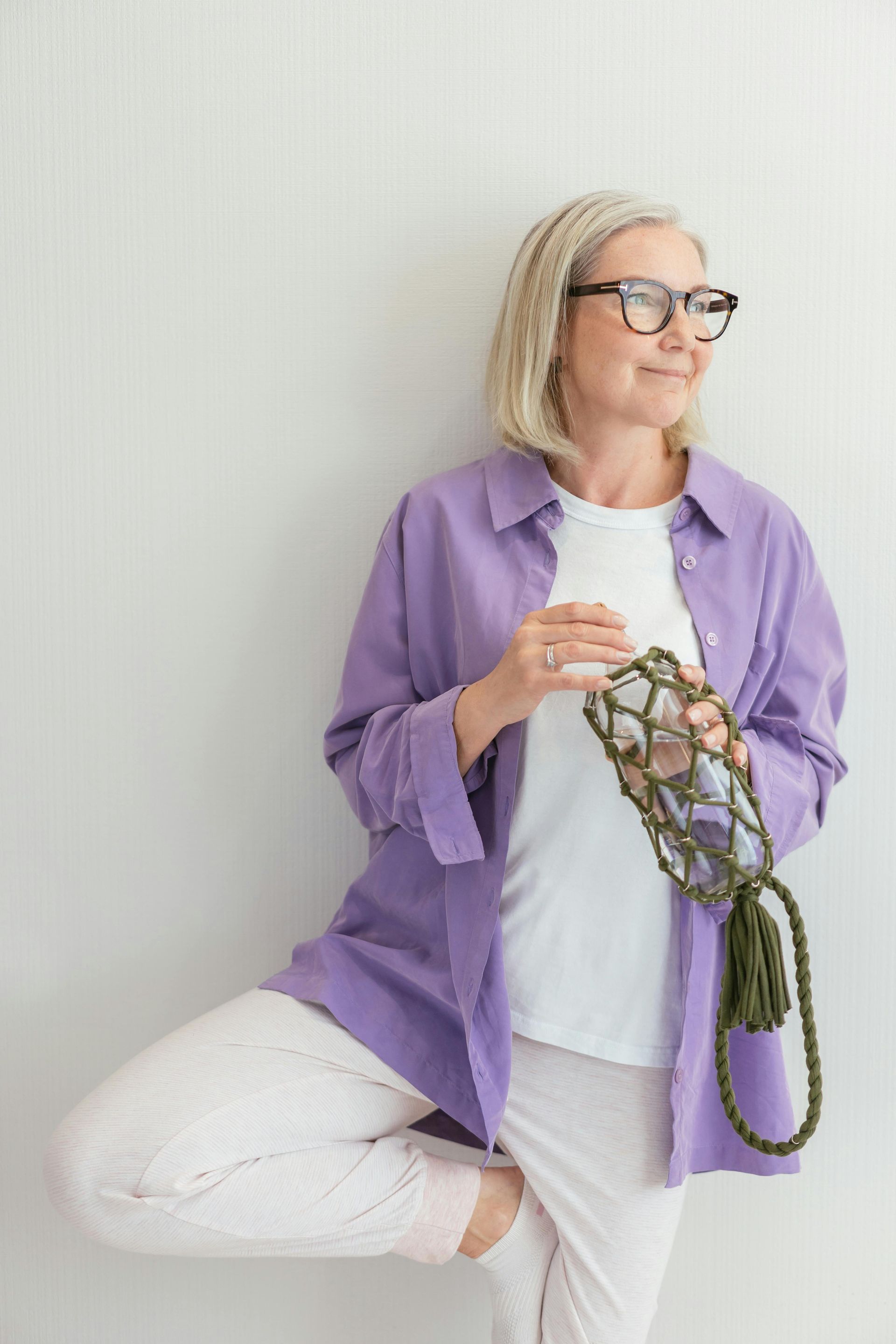 A woman in a purple shirt and white pants is standing in a yoga pose.