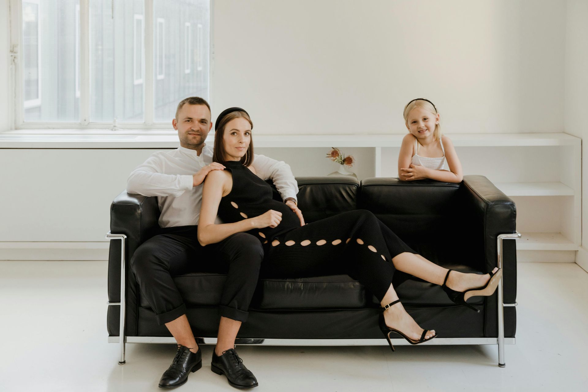 A man , a woman and a little girl are sitting on a black couch.