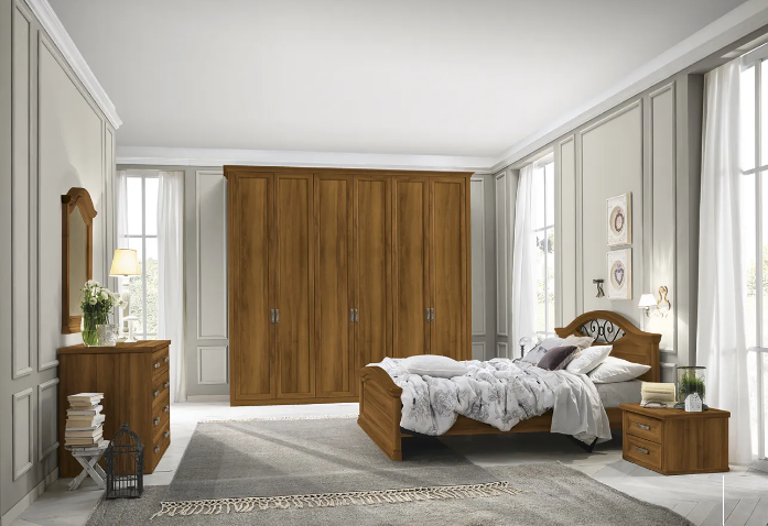 Camera da letto con mobili in legno: letto, cassettiera, comodino e ampio armadio. Pareti dai colori neutri, ampie finestre.