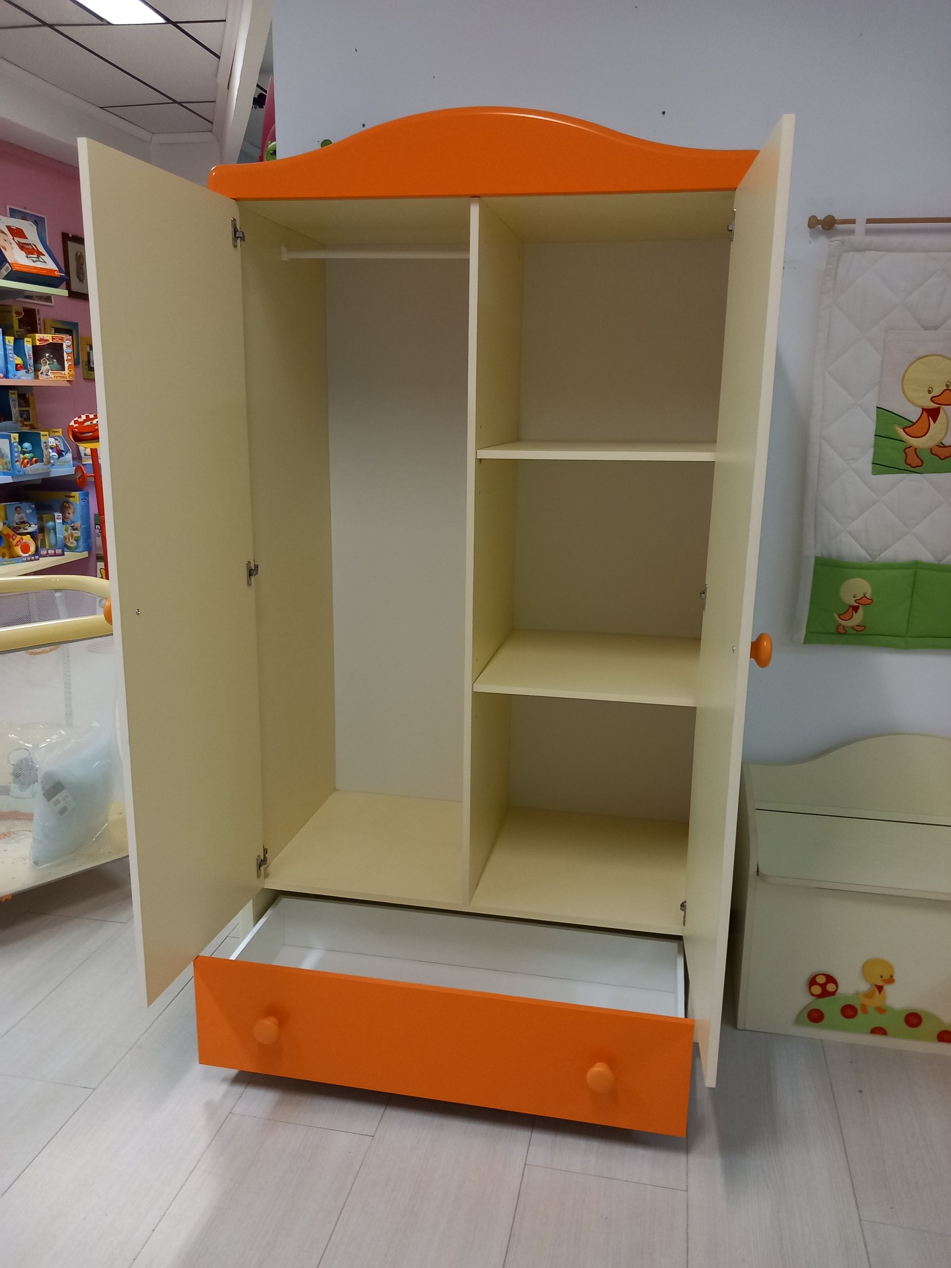 Armadio per bambini color arancione e crema con ante aperte, che mostrano un'asta appendiabiti, ripiani e un cassetto.