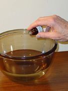 A person is holding a bottle of essential oil over a glass bowl.