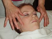 A woman is laying on a bed getting a massage on her face.