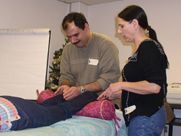 A man and a woman are standing next to a person laying on a bed.