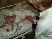 A woman is standing next to a baby in a hospital bed.