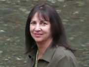 A woman in a green jacket is standing in front of a river.