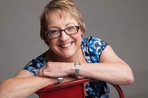 A woman wearing glasses is sitting in a red chair and smiling.