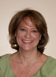 A woman wearing a green shirt and a gold necklace smiles for the camera.