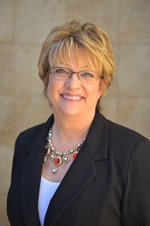 A woman wearing glasses and a necklace is smiling for the camera.