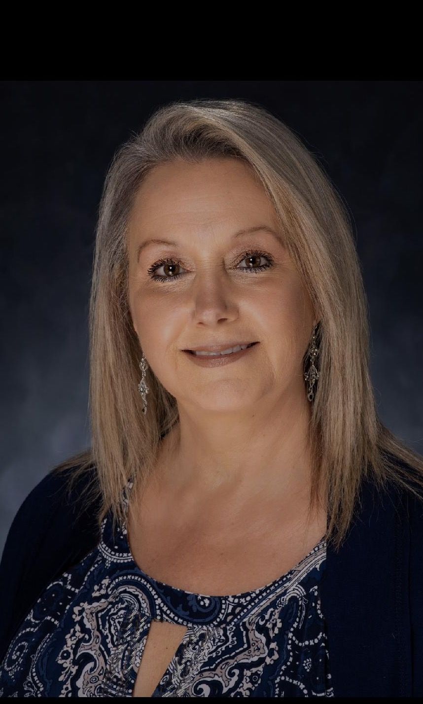 A woman wearing a blue shirt and a blue cardigan is smiling for the camera.