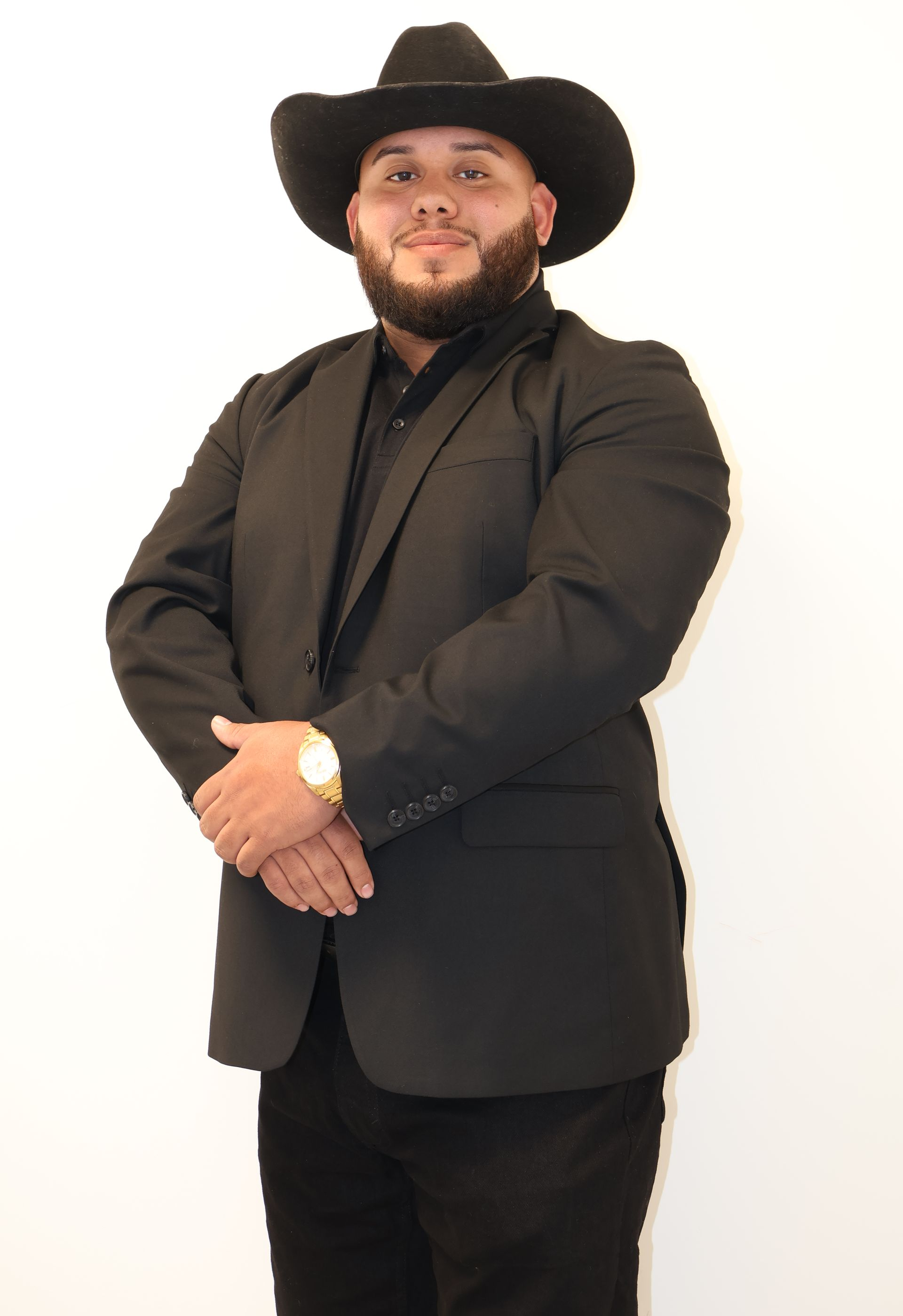Man wearing a black cowboy hat and suit, arms crossed, gold watch.