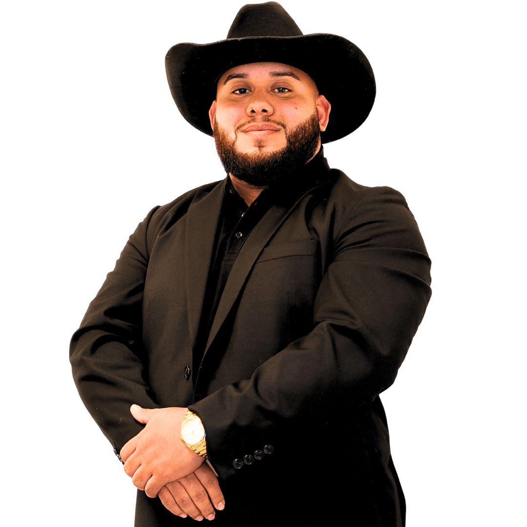 Man in a black suit and cowboy hat, arms crossed. He has a beard and is smiling.