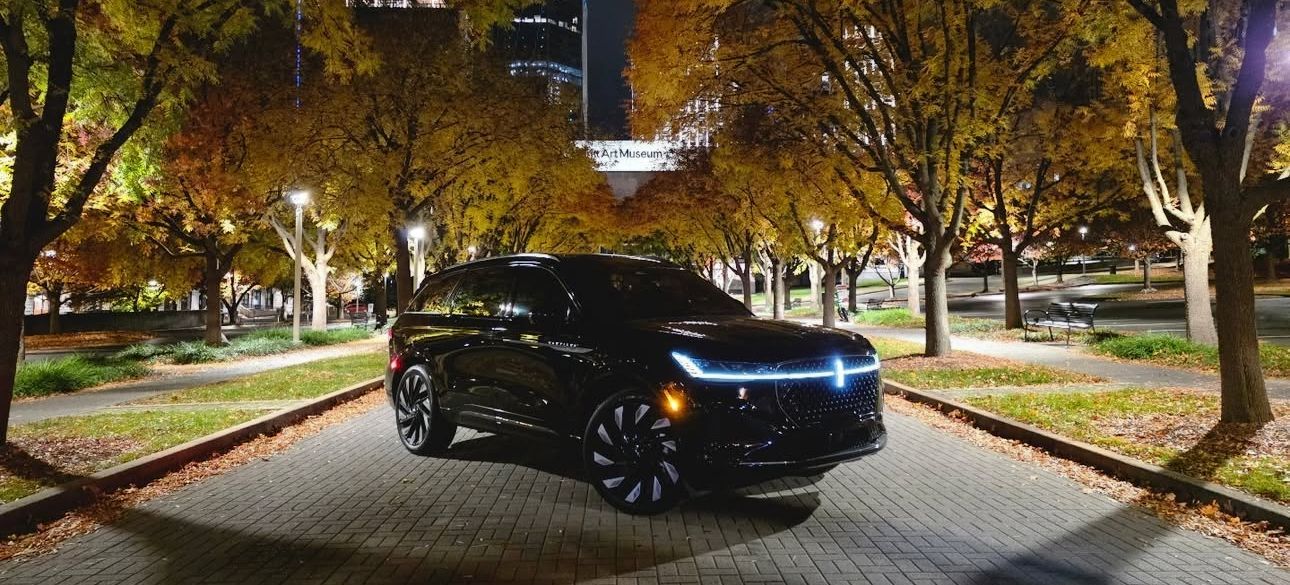 Black Lincoln SUV parked on a brick road lined with trees at night.