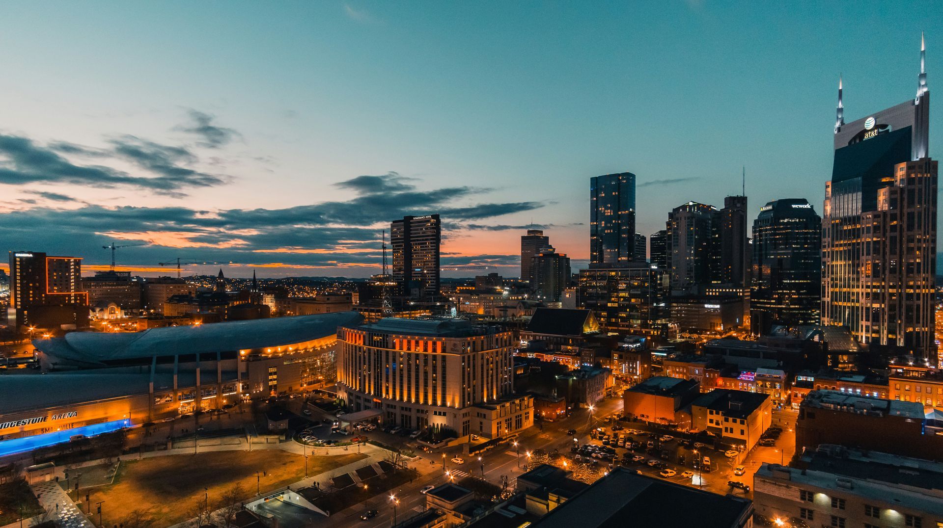 Nighttime cityscape of Nashville, TN, with lit buildings under a twilight sky.