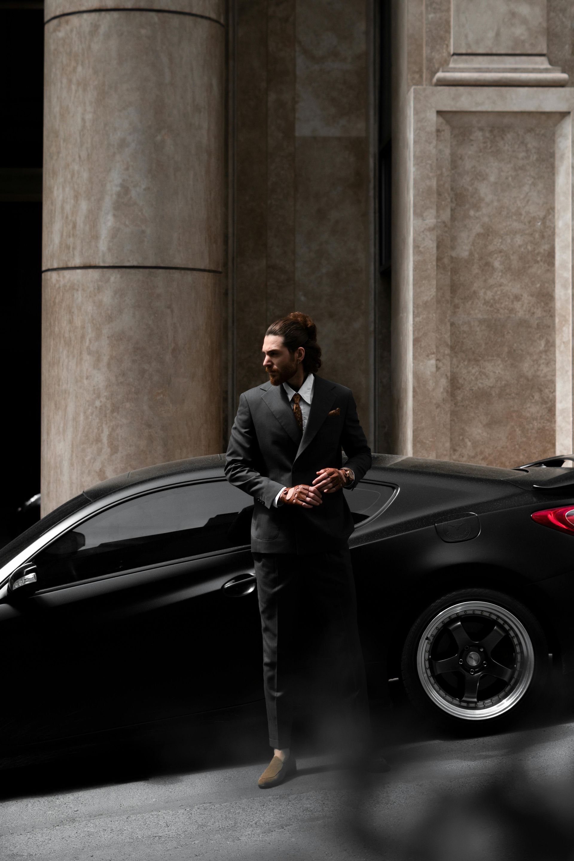 Man in suit leans against a black car near a building.