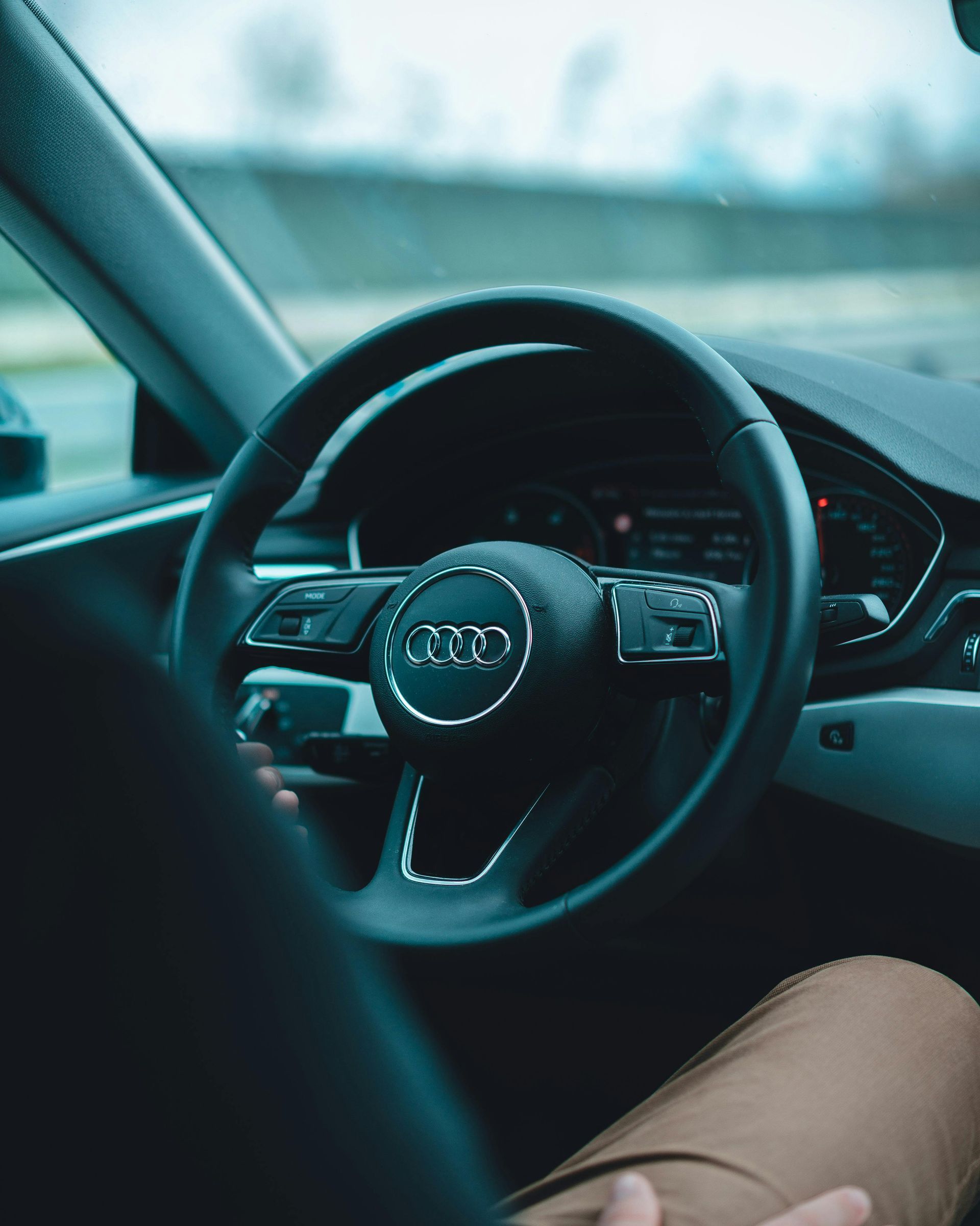 Audi car interior with steering wheel, dashboard, and driver's hands visible.