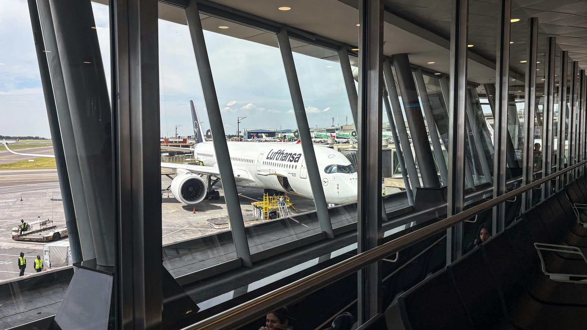 Man loading suitcase into car trunk; woman smiles nearby, sunny day.