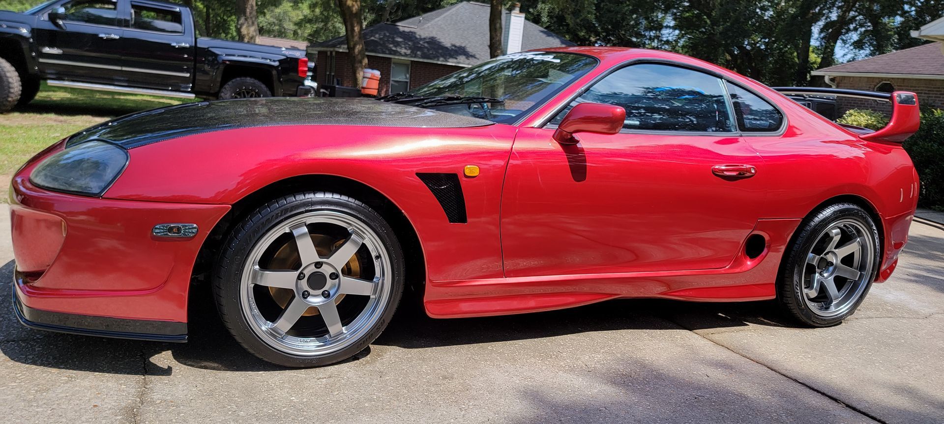 A red sports car is parked in a driveway next to a black truck.