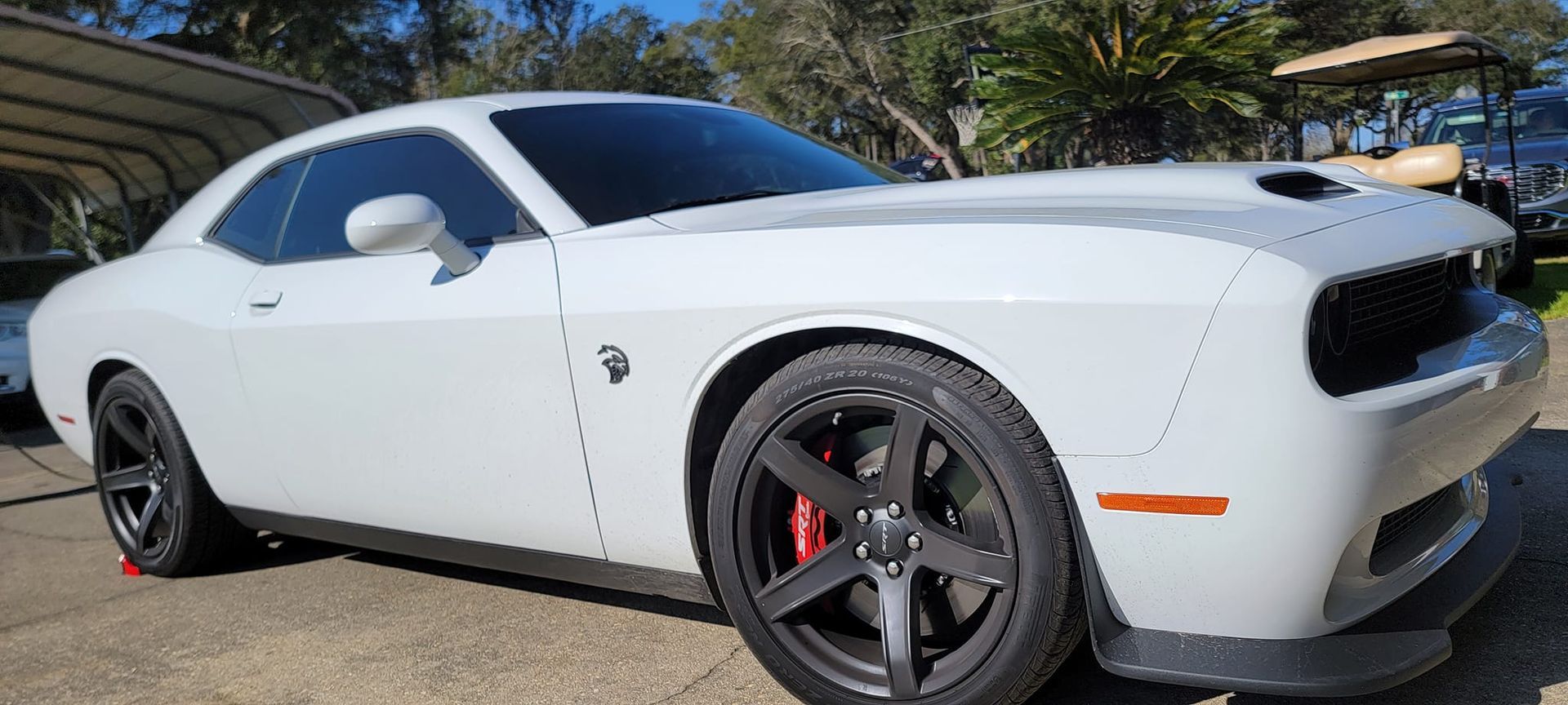A white dodge challenger srt hellcat is parked in a parking lot.