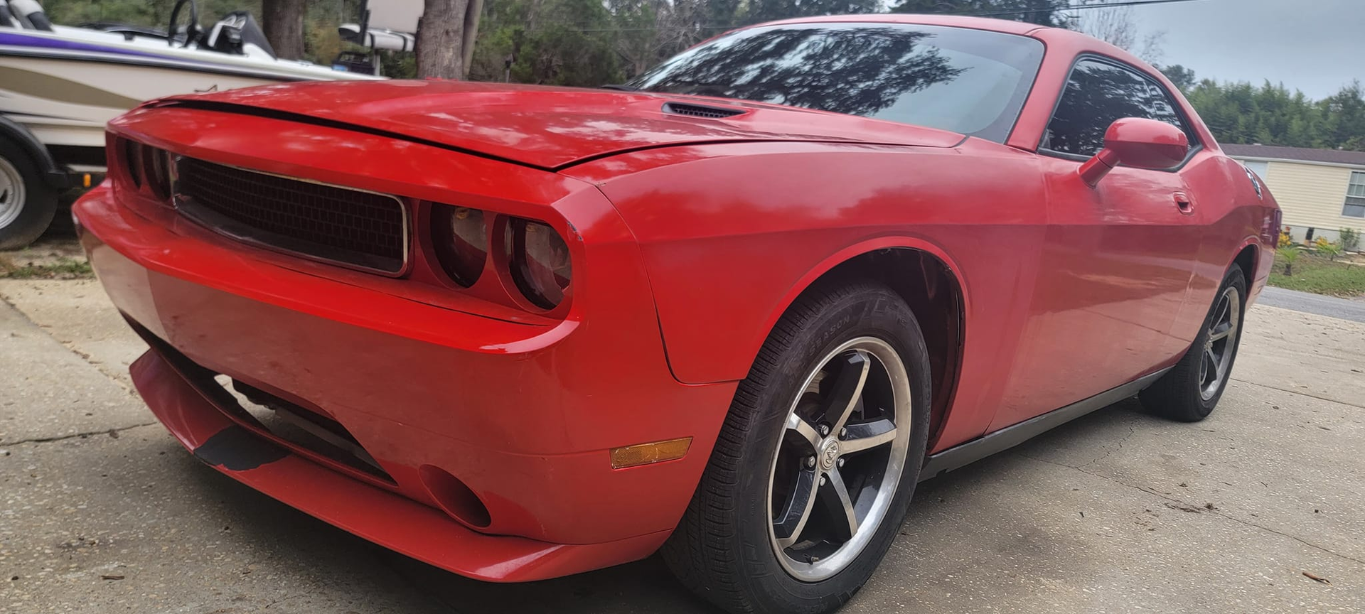 A red dodge challenger is parked in a driveway next to a boat.