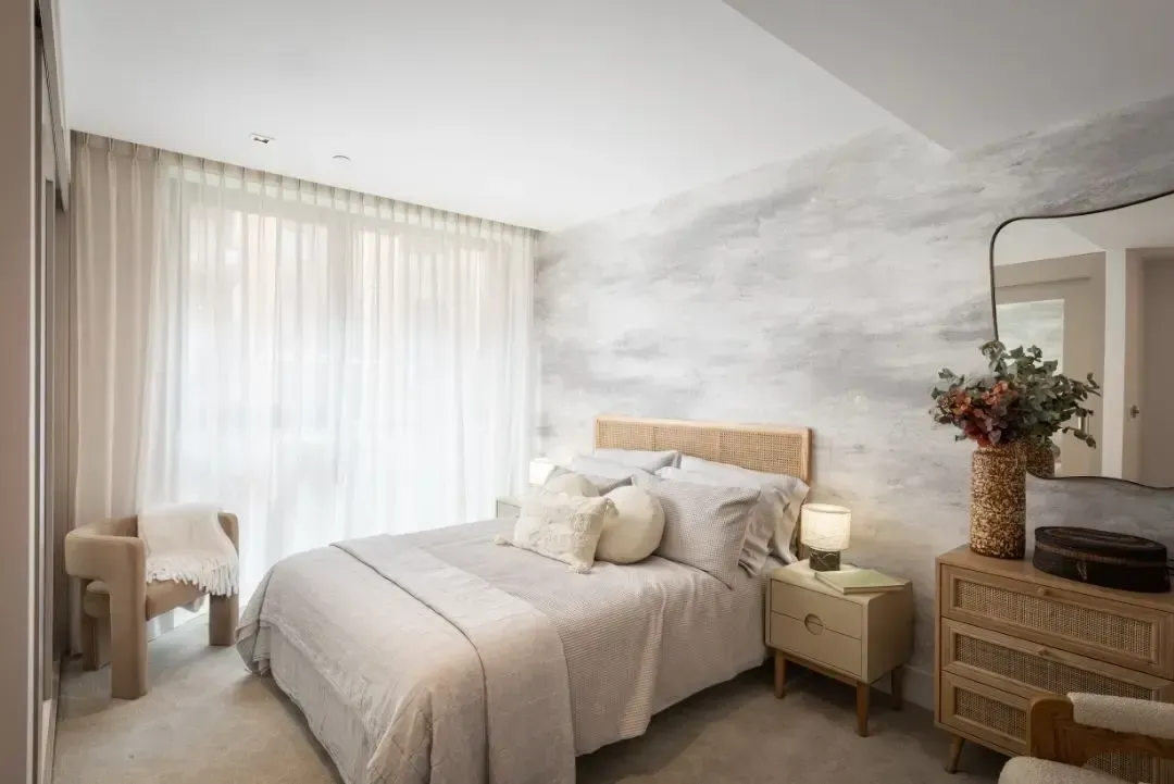 Modern bedroom with a neatly made bed, beige quilt, blue curtains, and bedside lamp