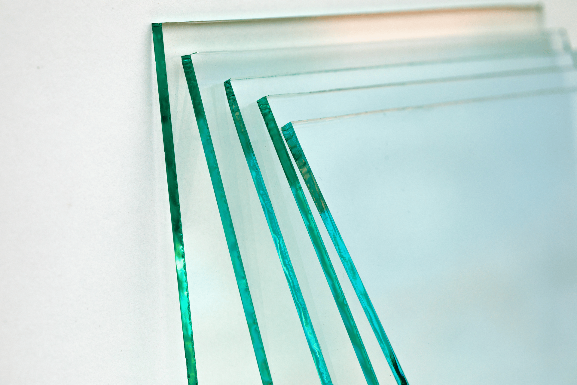 Clear glass sheets stacked against a white background, edges showing a slight green tint.
