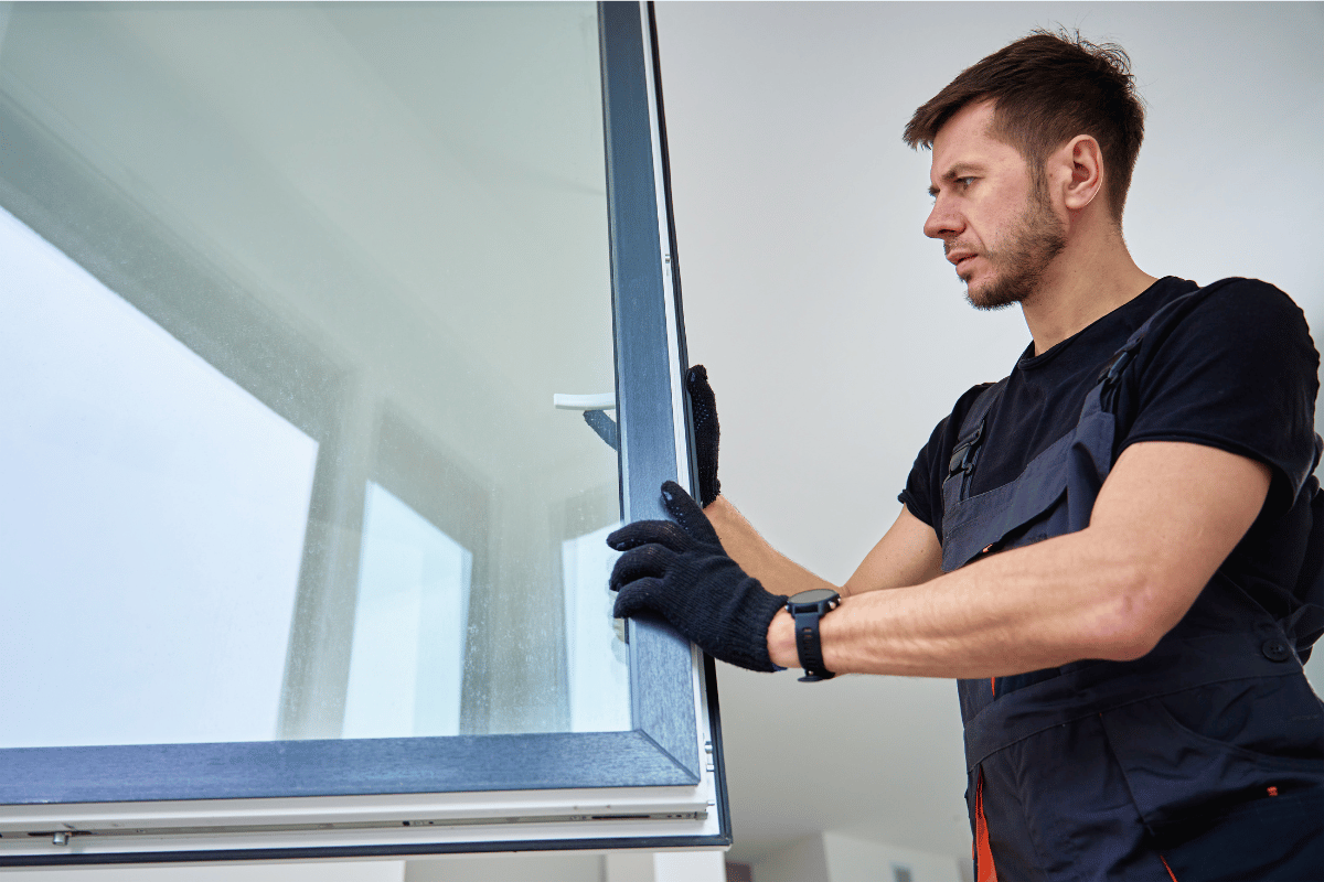Man in work clothes installing a window, indoors.