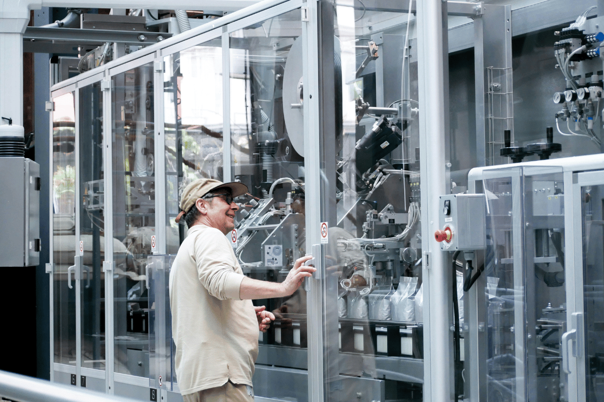Woman in a factory checking a packaging machine, smiling.