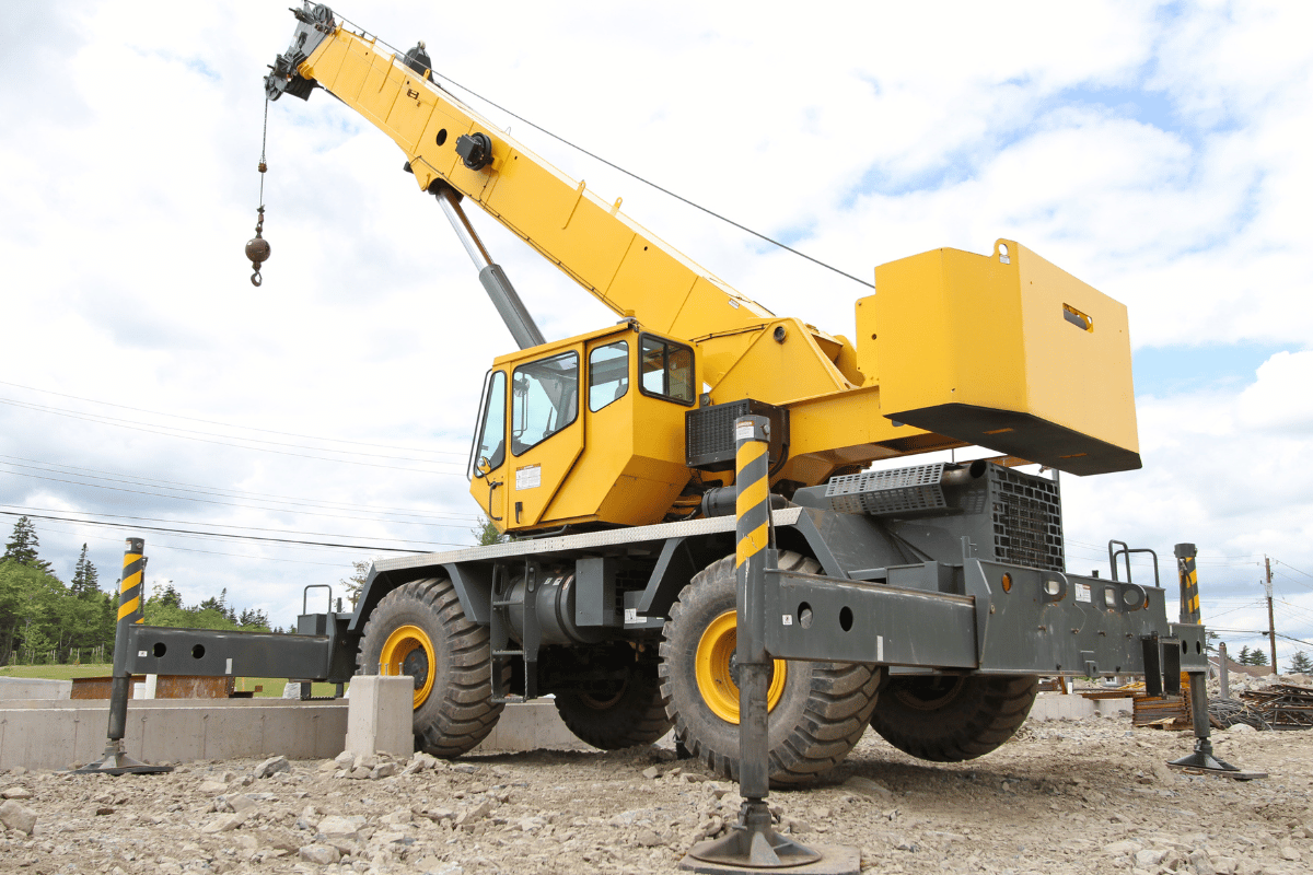 Yellow mobile crane on a construction site, with boom extended, resting on stabilizers.