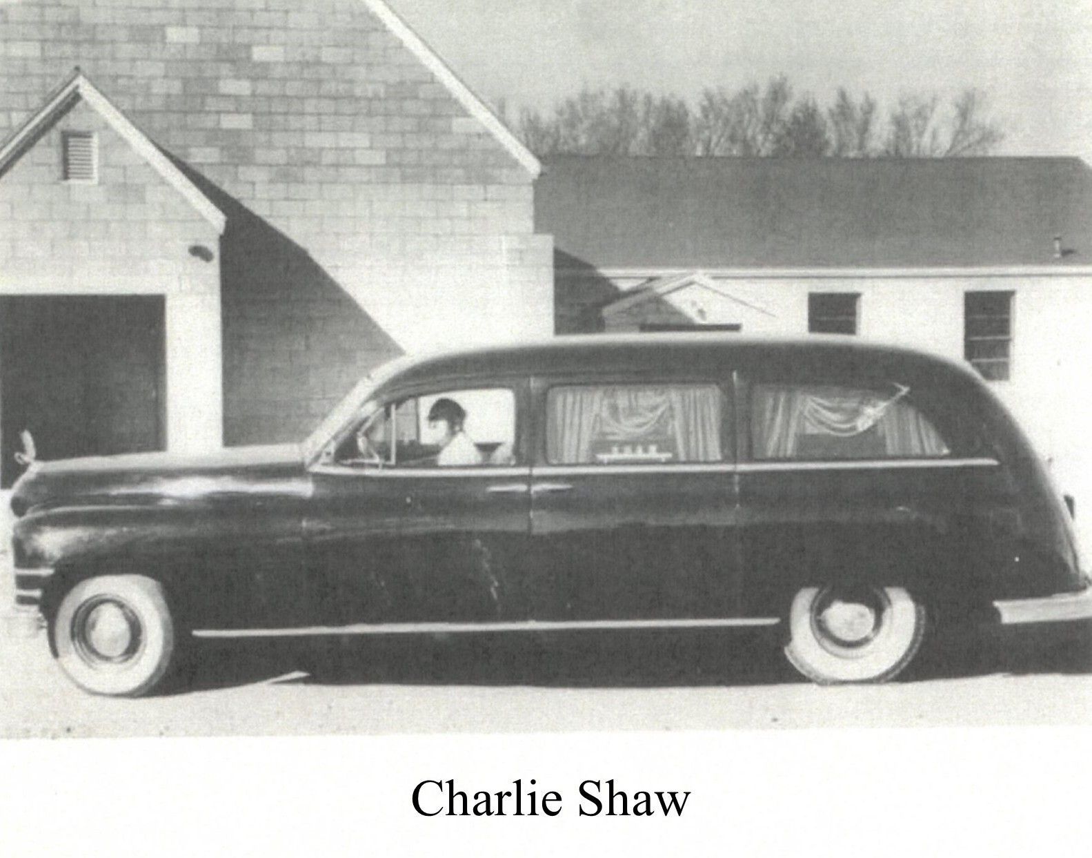 Black hearse parked in front of a building; driver visible.
