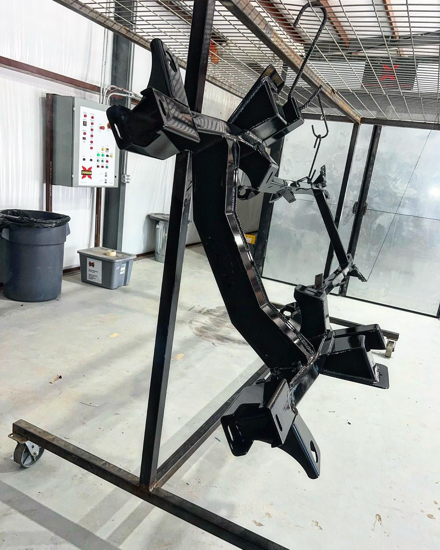 Black metal frame suspended on a rack in a spray booth, ready for painting.
