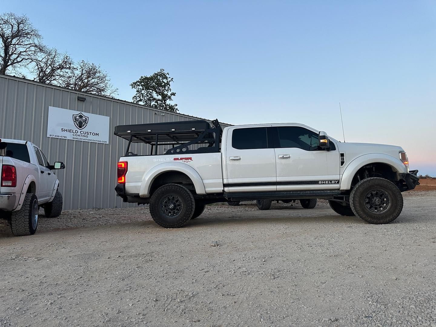 White lifted truck with black wheels and camper shell parked near a building.