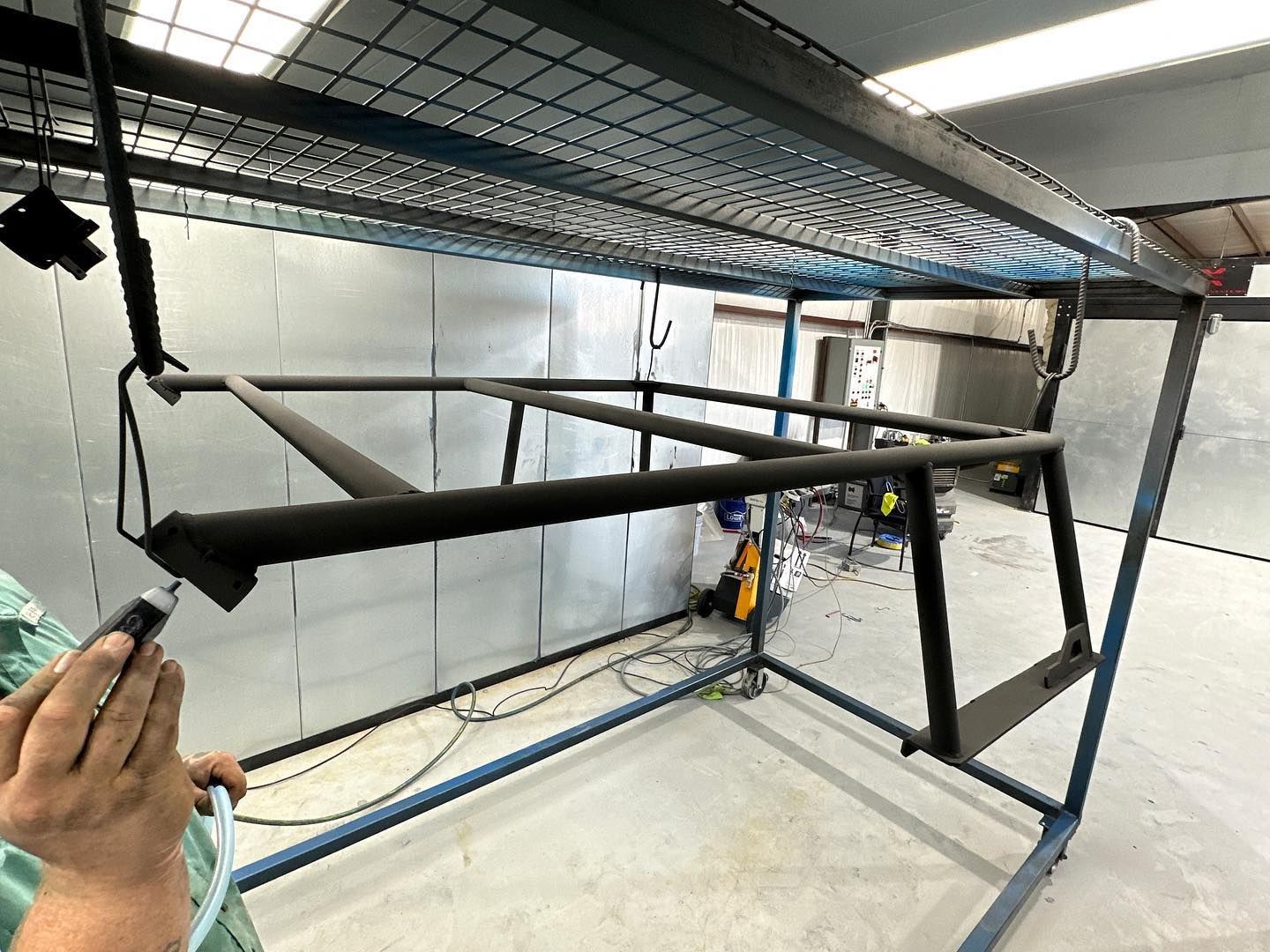 A person sprays a black metal frame with a spray gun inside a spray booth.