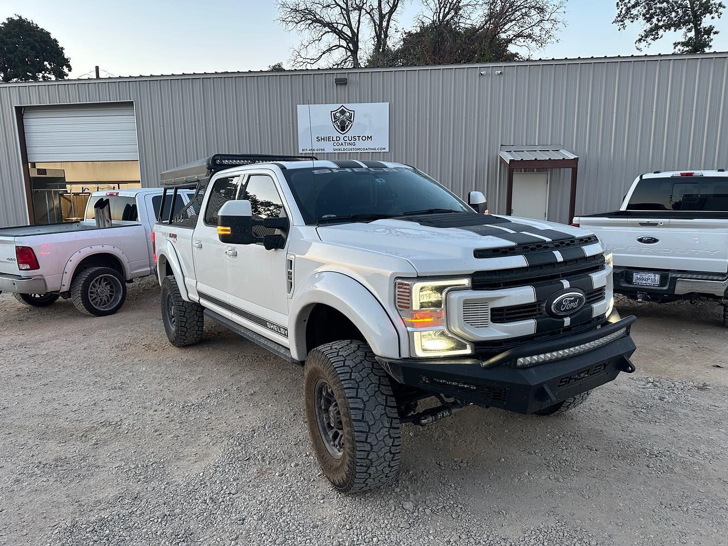 White Ford pickup truck with black stripes parked outside a building. Other vehicles are visible.