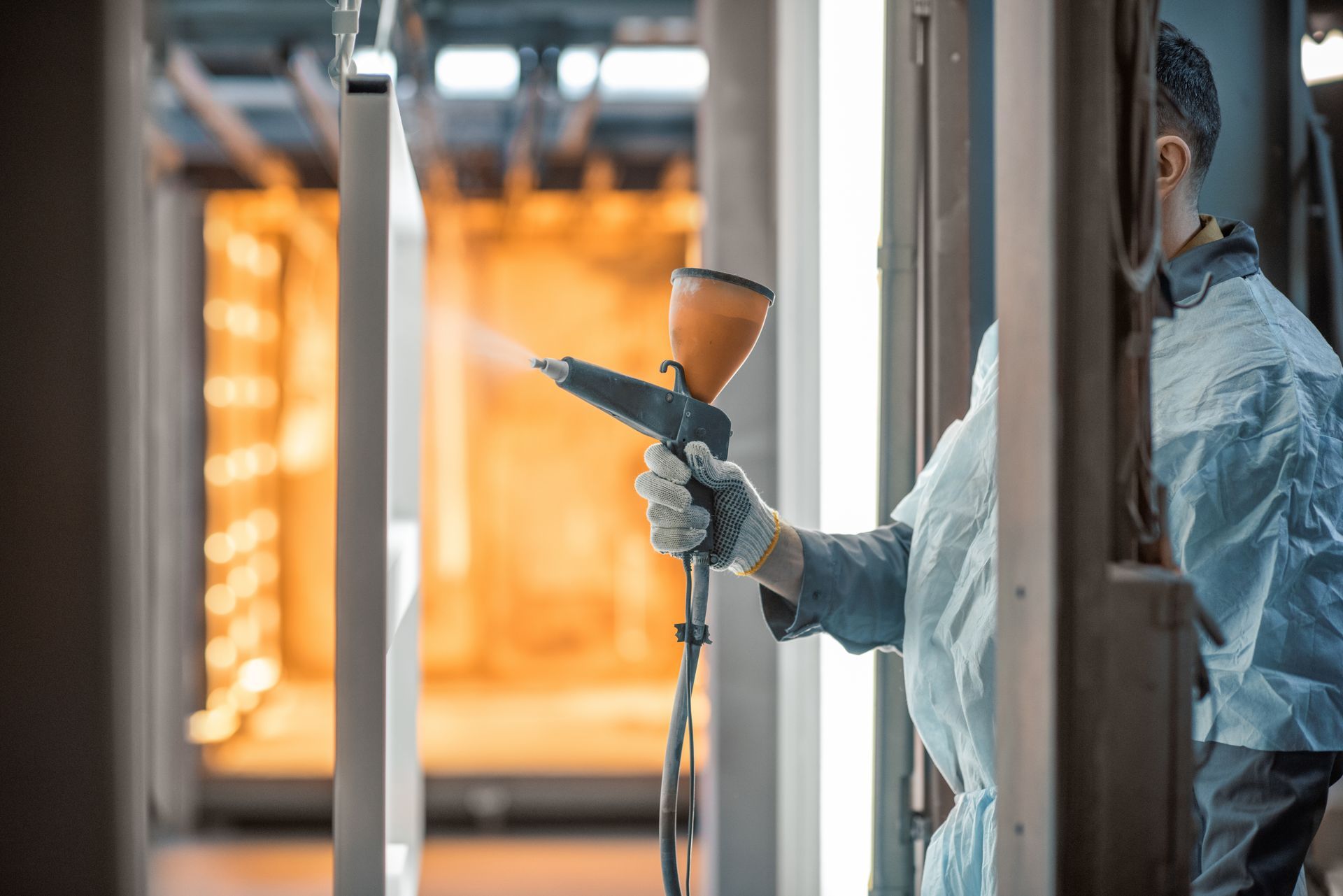 Person spraying paint inside a factory; the setting has an orange glow.