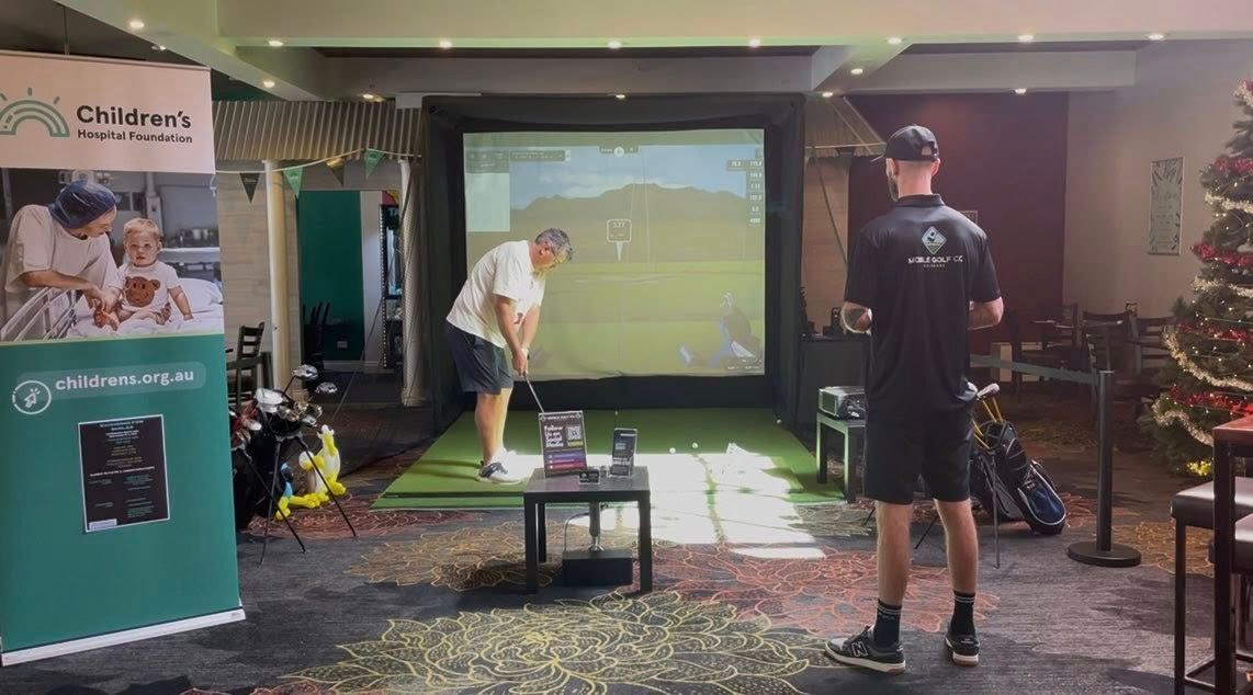Man golfing on an indoor simulator; Mobile Golf Co staff observing. 