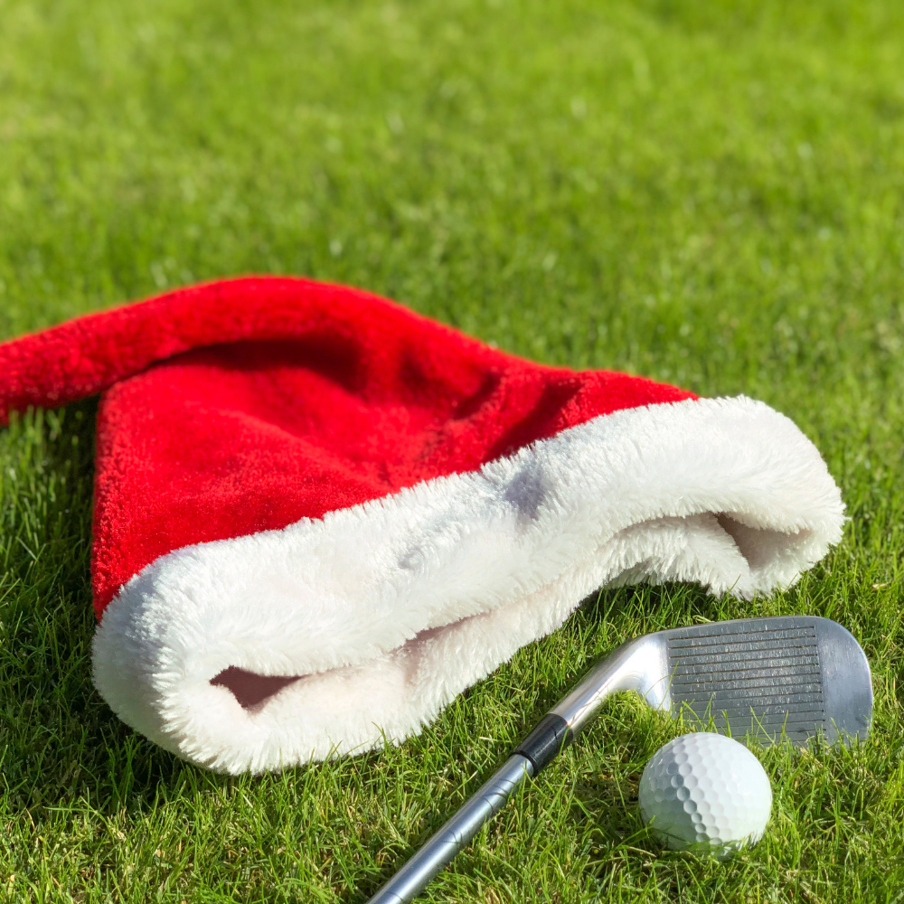 Santa's hat on the grass next to a golf club and ball.