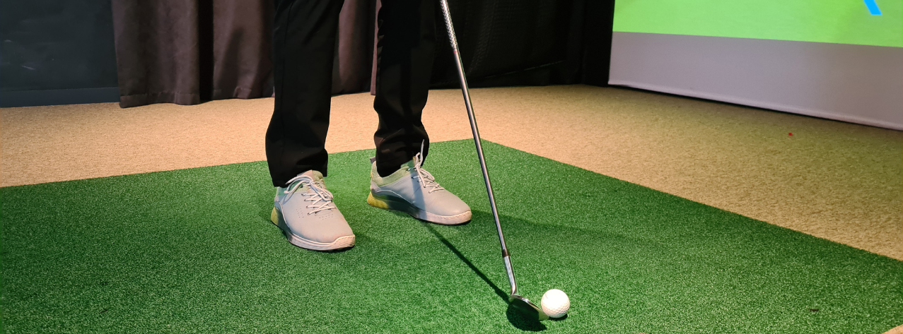 person standing on a tuf mat in front of a golf simulator screen with a ball resting infont of his golf club