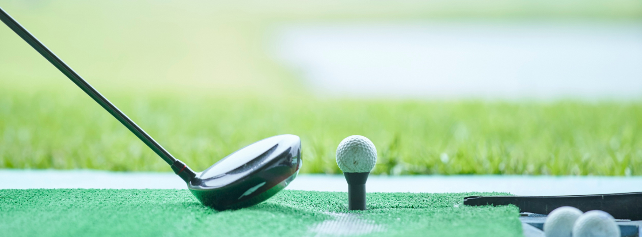 a golf driver resting on a mat next to a golf ball on a tee, ready to be hit down the range.