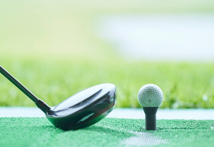 A golf driver club resting on a mat next to a golf ball on a tee, ready to be hit.