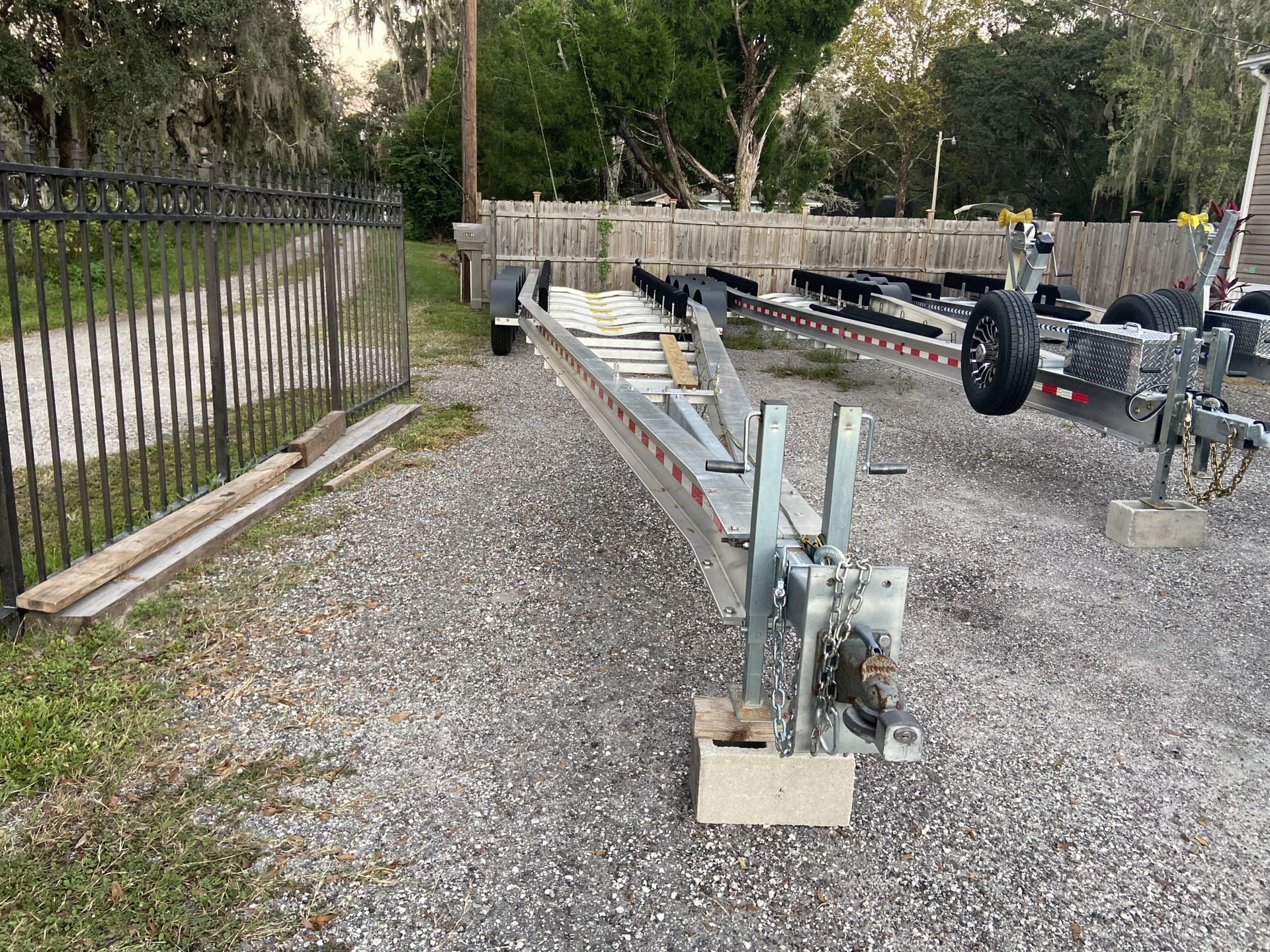 A boat trailer is parked in a gravel lot next to a fence.