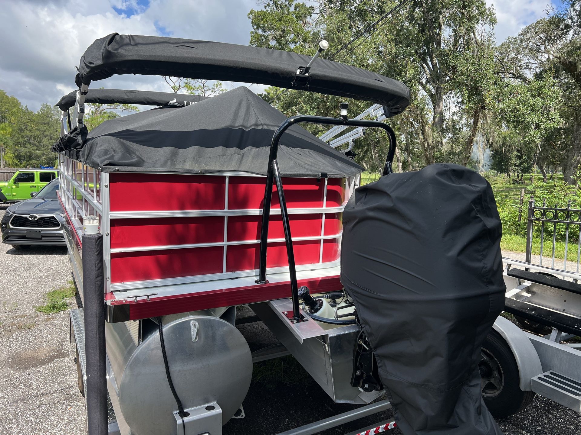 A red pontoon boat with a black cover on the back is parked on a trailer.