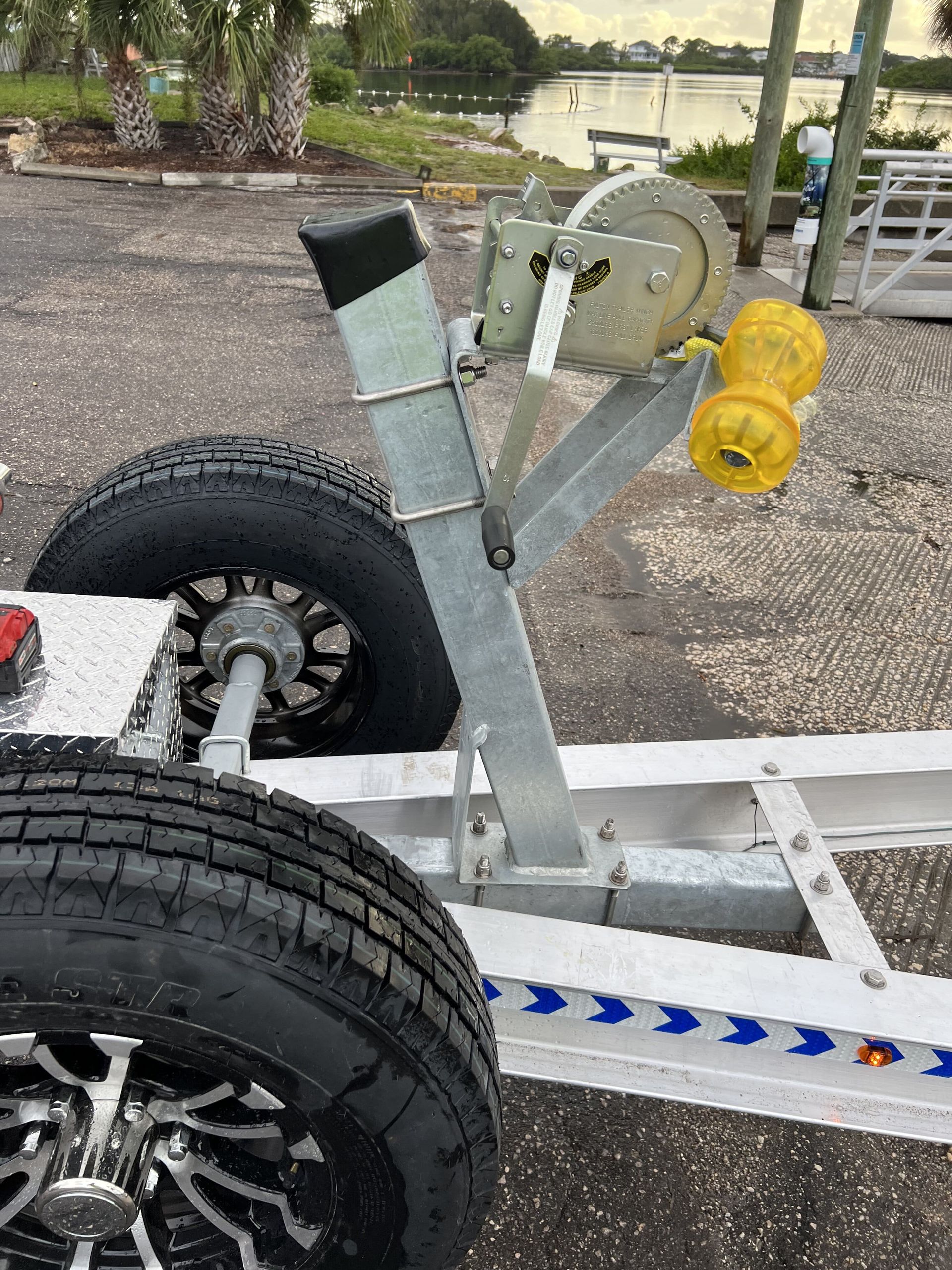 A boat trailer is parked in a parking lot next to a body of water.
