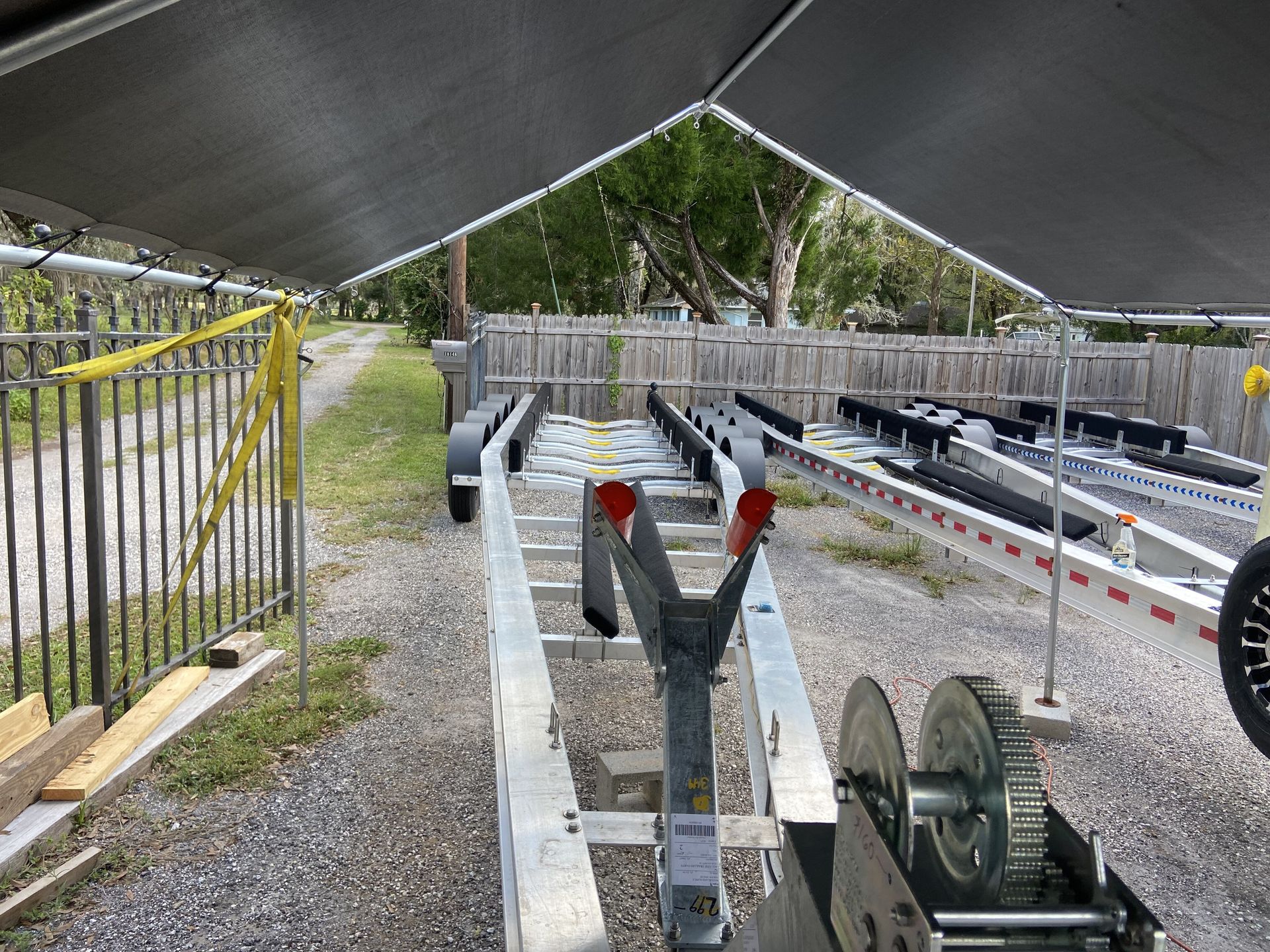 A boat trailer is parked under a canopy on a gravel road.