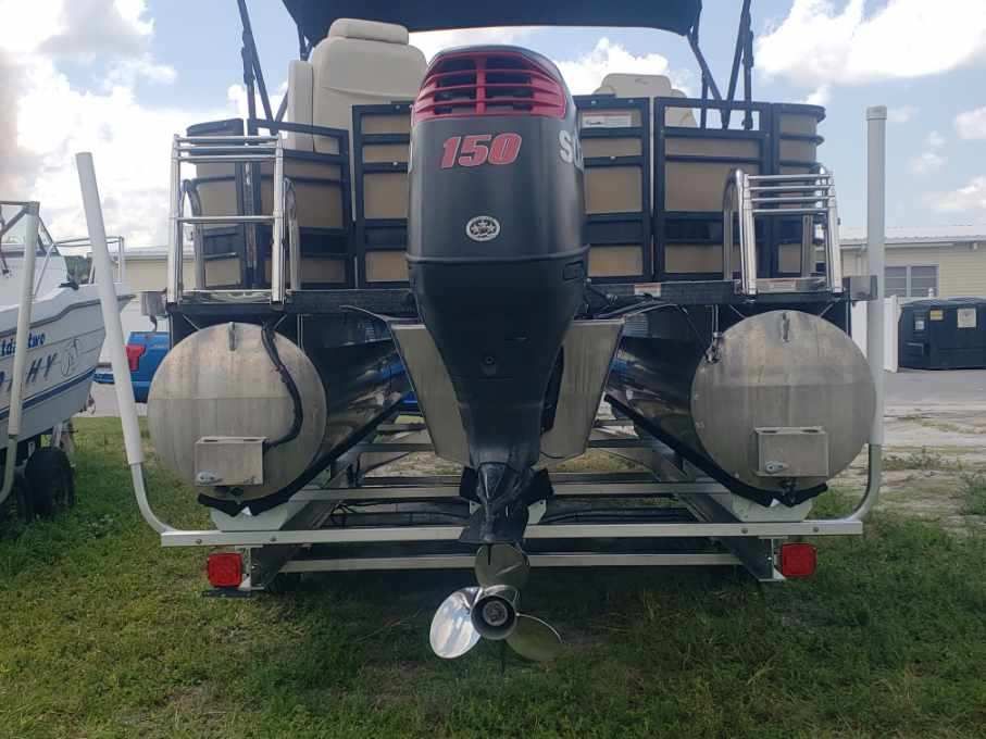 A pontoon boat with a mercury outboard motor is parked in the grass.