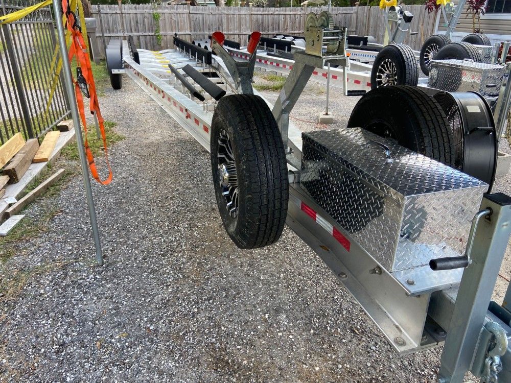 A boat trailer is parked on gravel in front of a fence.