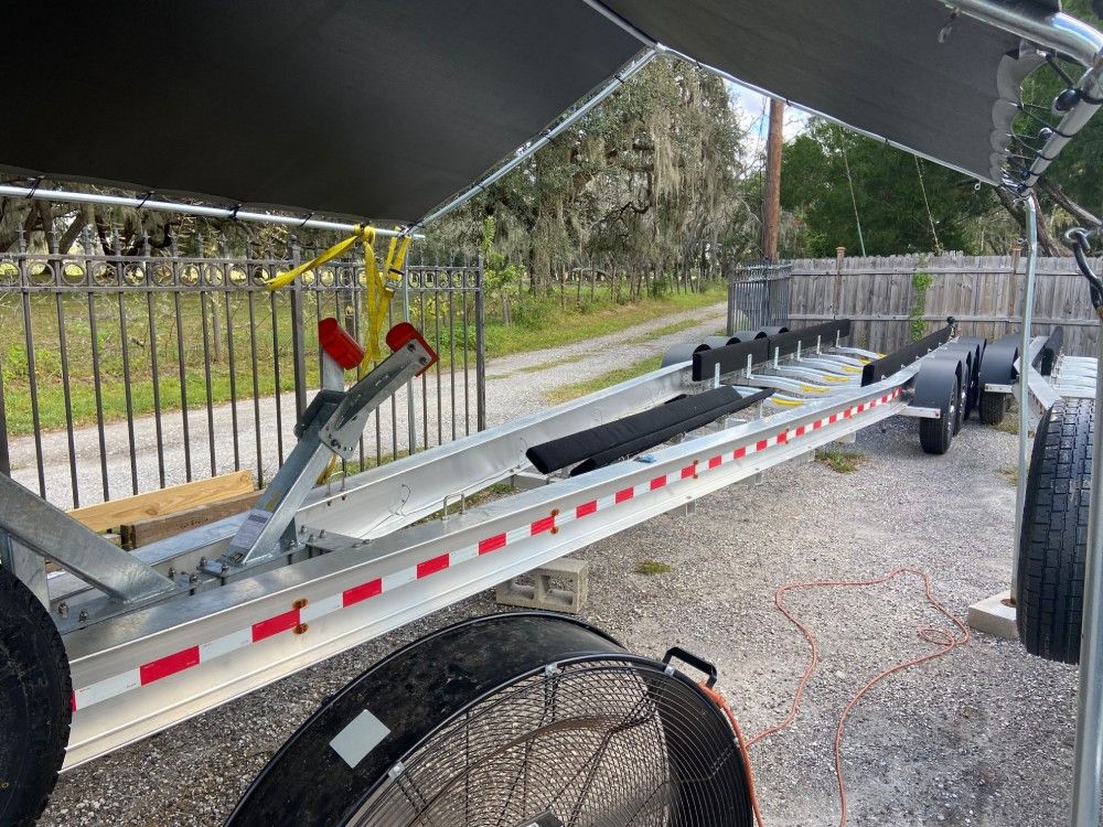 A boat trailer with a fan attached to it is parked next to a fence.